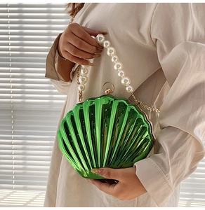 Detail of green shell clutch bag with pearl handle and golden chain on a model