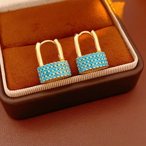 Detailed close-up of golden lock-shaped earrings with turquoise stones in a velvet box