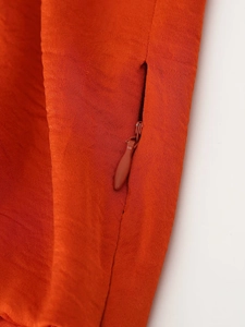 Close-up of the hidden zipper detail on the orange satin dress with textured fabric