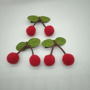 Detail of three handmade plush cherry hair clips with red pom-poms and green felt leaves