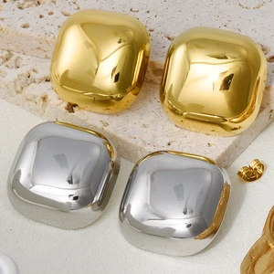 Macro view of polished square gold and silver stud earrings on a natural stone background