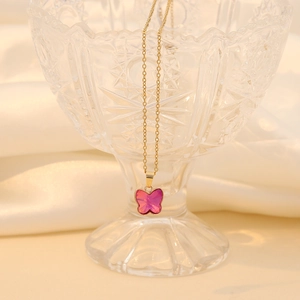 Pink glass butterfly pendant on gold stainless steel chain draped over a glass bowl