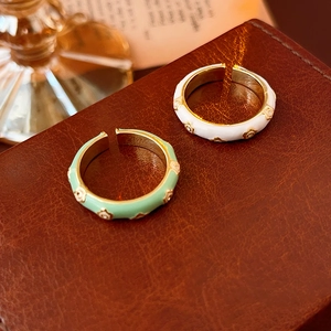 Dettaglio di anelli a fiore in smalto vintage regolabili in verde e bianco su pelle