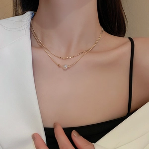 Close-up of elegant gold layered necklace with small beads and white pearl pendant on model