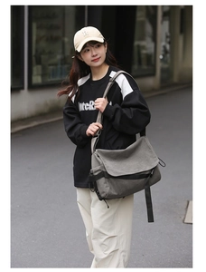 Grey canvas messenger bag worn by male model in a stylish outdoor streetwear setting
