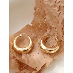 Detailed close-up of thick C-shaped gold hoop earrings with polished finish on honeycomb paper
