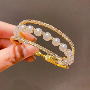 Detailed close-up of a triple-layer bangle featuring gold bands, crystals, and white pearls