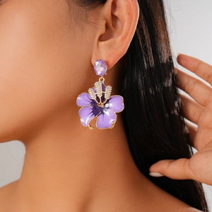 Detail of purple flower drop earring with crystals and gold edge on a female model