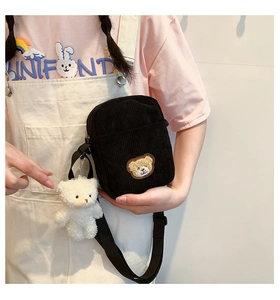 Detail of black corduroy crossbody bag with yellow bear patch and plush charm