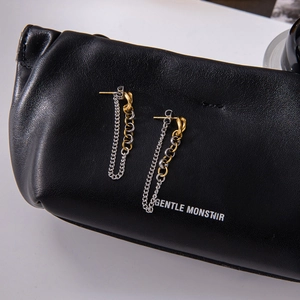 Détail de boucles d'oreilles bicolores dorées et argentées sur fond de cuir noir texturé