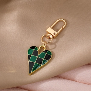 Detail of a gold-plated heart keychain with green and black checkerboard enamel pattern
