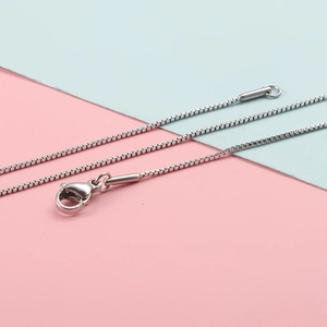 Detail van een zilveren boxketting met een stevige kreeftsluiting op een tweekleurige achtergrond