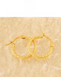 Detailed close-up of golden spiral texture hoop earrings on a soft textile background