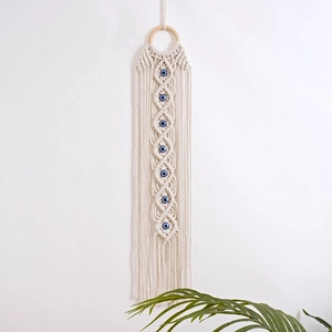 Detail of hand-woven macrame wall hanging featuring blue evil eye patterns and cotton fringe