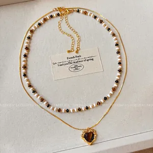 Detail of beaded necklace and gold heart pendant with tiger eye stone inlay