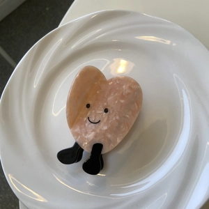 Pinza per capelli a cuore in acetato con faccina sorridente su un piatto di ceramica