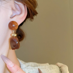 Detail of vintage caramel resin geometric drop earrings worn with gold accents
