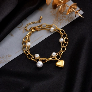 Double-layered gold chain bracelet featuring white pearls and a heart pendant charm