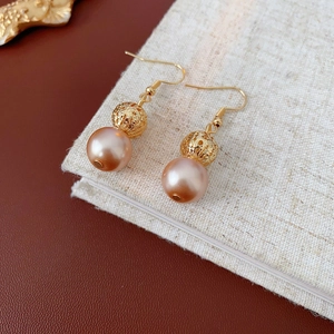Macro detail of gold hollow-out floral beads and rose gold pearl earrings on linen