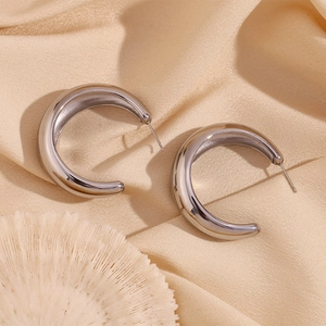 Polished silver stainless steel crescent hoop earrings resting on beige textured fabric