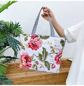Detail of floral tote bag showing large pink peony prints and grey handles held by a hand