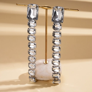 Macro view of crystal rhinestone rectangle drop earrings on golden T-bar display stand