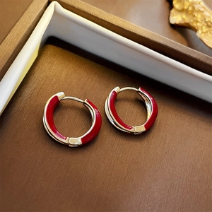 Close-up of vintage C-shaped earrings with red enamel and gold finish on a tray