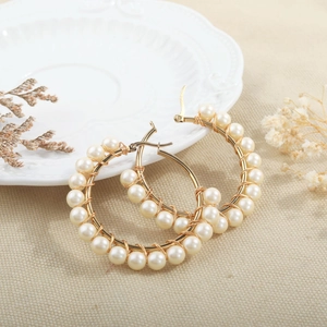 Detail of beaded pearl hoop earrings with gold wire on a textured beige fabric background