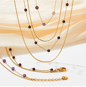Detail of layered stainless steel necklace with gold chain and natural purple beads