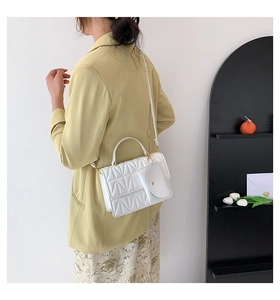 Close-up of white quilted handbag with diamond pattern and detachable round pouch charm