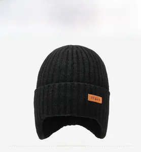 Detail van zwarte gebreide muts met fleecevoering, oorkleppen en leren logo-patch