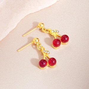 Detail of red cherry pendant earrings with rhinestone leaf on beige silk background