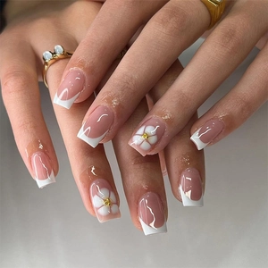 Detail of square nude French press-on nails with 3D white floral and gold center accents