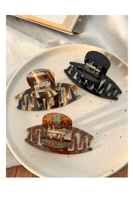 Detailed view of three acrylic hair claws in black, tortoiseshell and amber on a beige plate