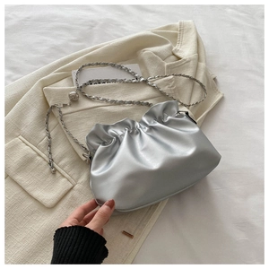 Close-up of metallic silver pleated cloud bag with chunky woven chain strap on a blazer