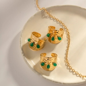 Vue macro de trois bagues martelées dorées avec malachite verte sur plateau céramique