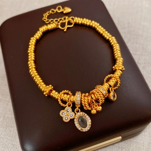 Close-up of gold beaded bracelet with oval gemstone, clover charm and heart pendant