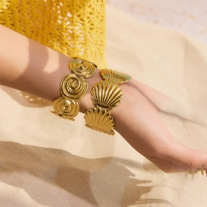 Golden stainless steel spiral and shell bangles on wrist for a beach jewelry look