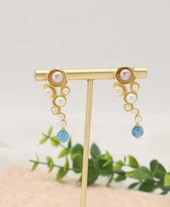 Detail of natural pearl earrings with blue gemstone drops on a golden jewelry stand