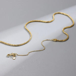 Macro detail of gold sparkling chain showing lobster clasp and star pendant on grey background