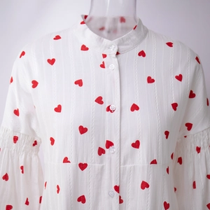 Détail du tissu en coton blanc avec motifs cœurs rouges, col montant et manches bouffantes