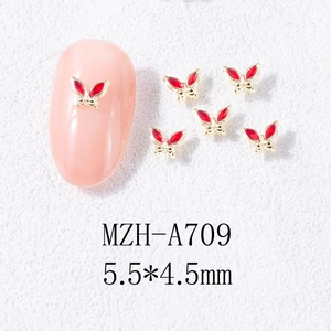 Macro detail of red butterfly nail charm with gold metal base measuring 5.5x4.5mm