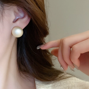 Close-up of a matte champagne pearl stud earring worn by a model for a French chic style