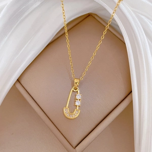 Gold safety pin necklace with cubic zirconia pendant on beige silk display box