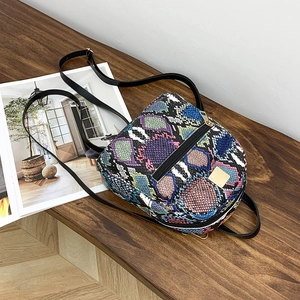 Detail of a mini backpack with multicolor snakeskin texture and gold hardware on wood