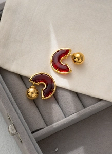 Makro-Detail der goldenen C-förmigen Quastenohrringe mit tiefrotem Harz-Inlay