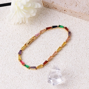 Gold chain bracelet with multi-colored rectangular zircons on a textured stone background