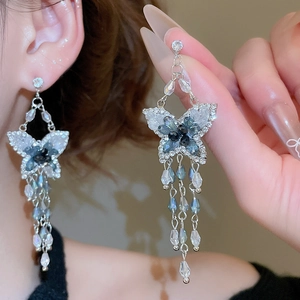 Détail de boucles d'oreilles papillon en argent avec cristaux bleus et pompons en perles