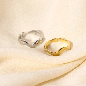 Anelli minimalisti placcati oro 18K con linee fluide ondulate su tessuto di seta