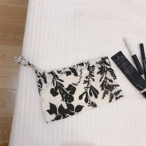 Gros plan d'une pochette en tissu à fleurs noir et blanc avec dragonne sur literie blanche